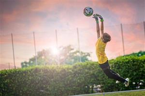 A Young Boy Goal Keeper Jumping For Soccer Ball